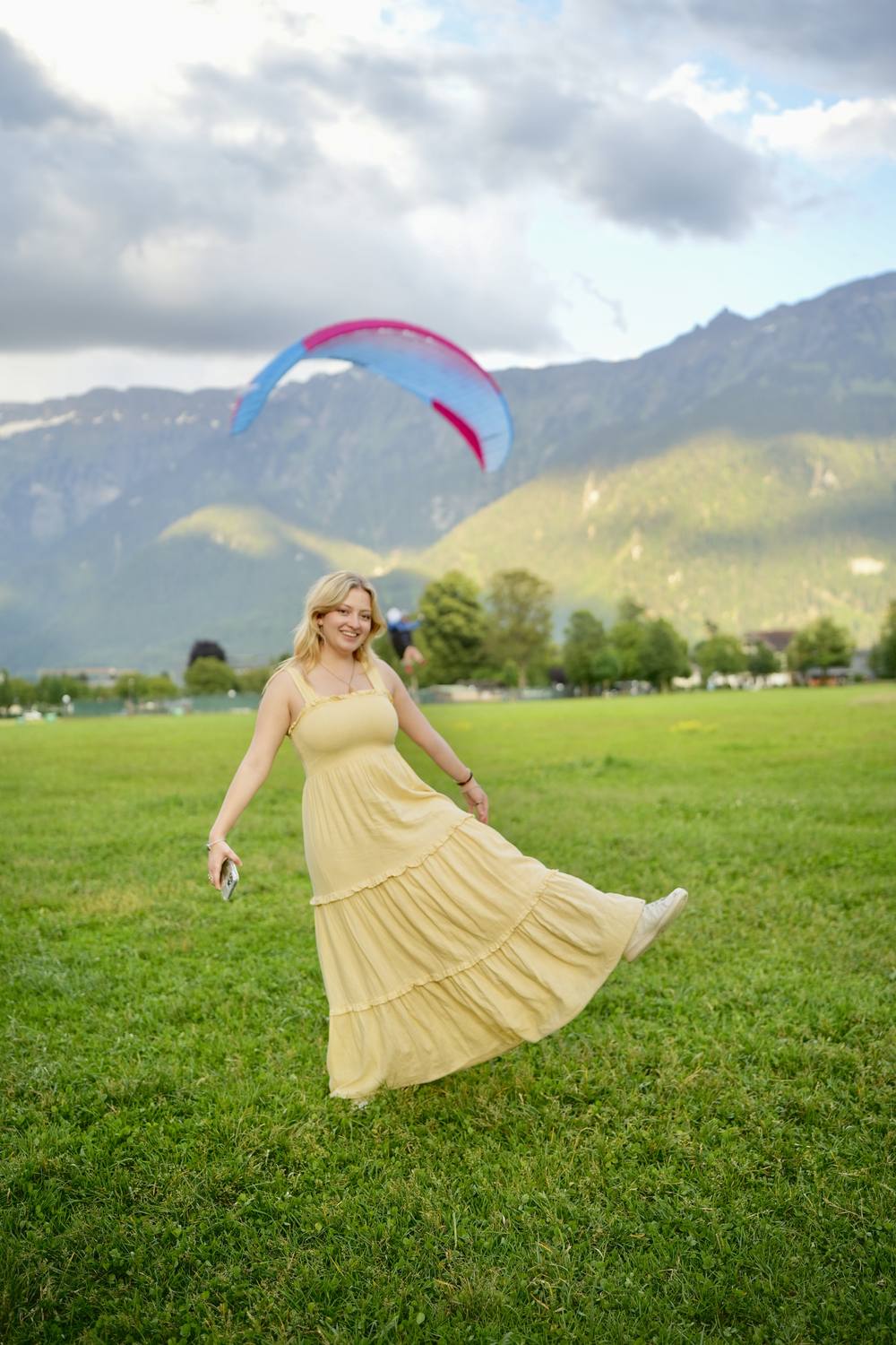A guest on the Hoehematte in Interlaken with a paraglider coming down behind her
