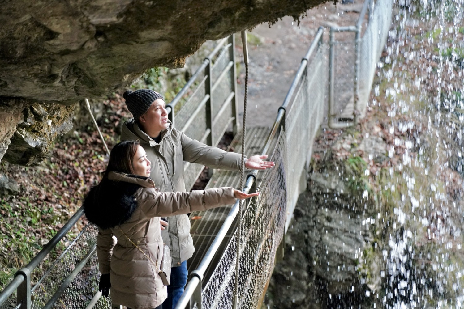 A couple on the walkway behind the Giessbach Falls, reaching into the falling water