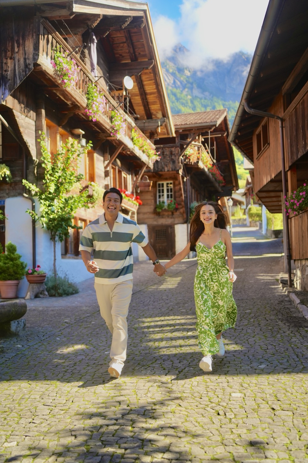 A couple running hand in hand through a lane of flower-decked wooden chalets in Brienz