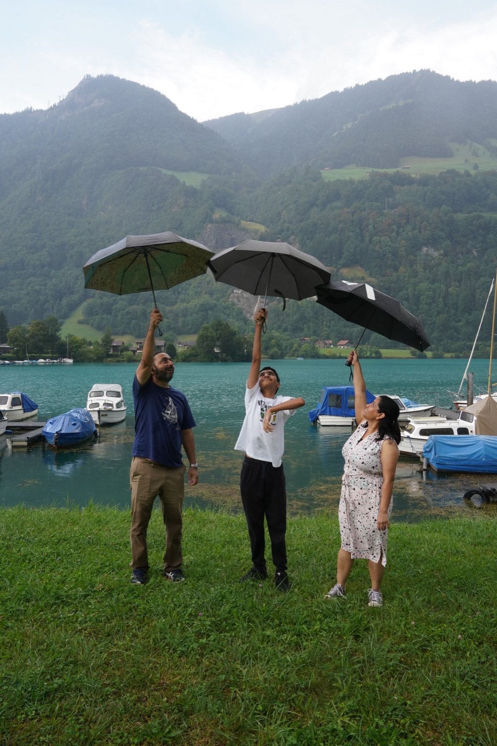 A family holding up umbrellas on a rainy day at the shore of Lake Brienz