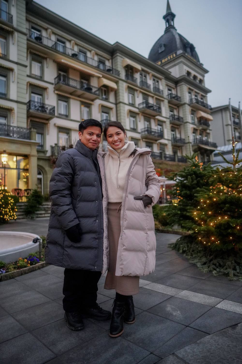 A couple in winter coats in front of the lit grand hotel on the Hoehematte in Interlaken
