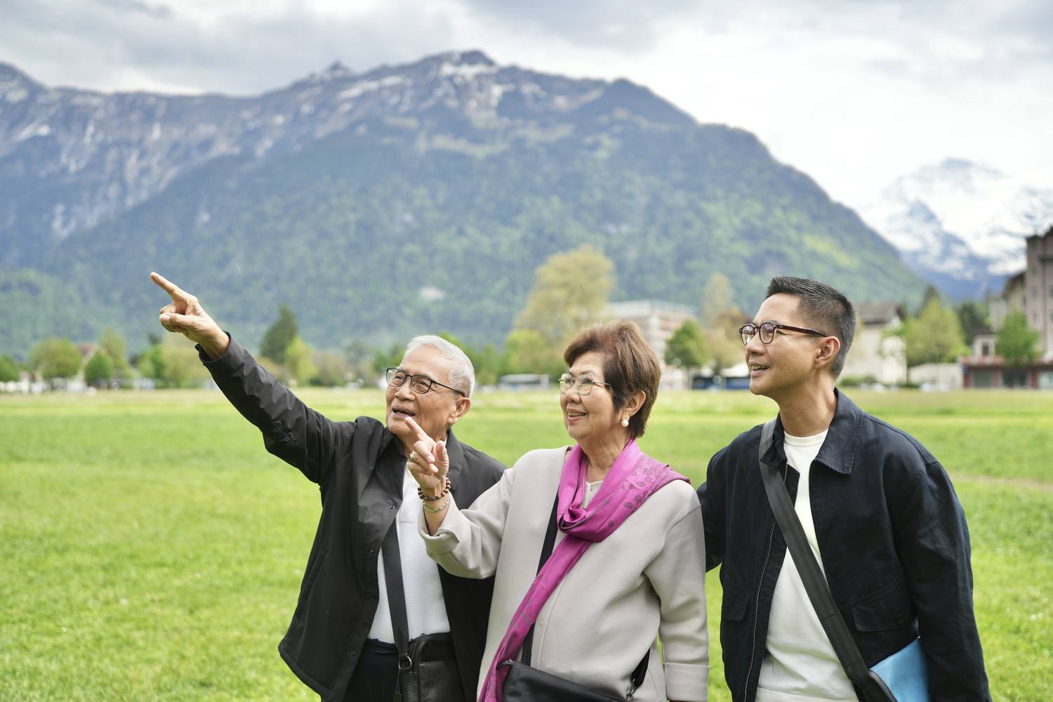 Three guests on the Höhematte meadow in Interlaken pointing out the peaks, with the Jungfrau in the distance
