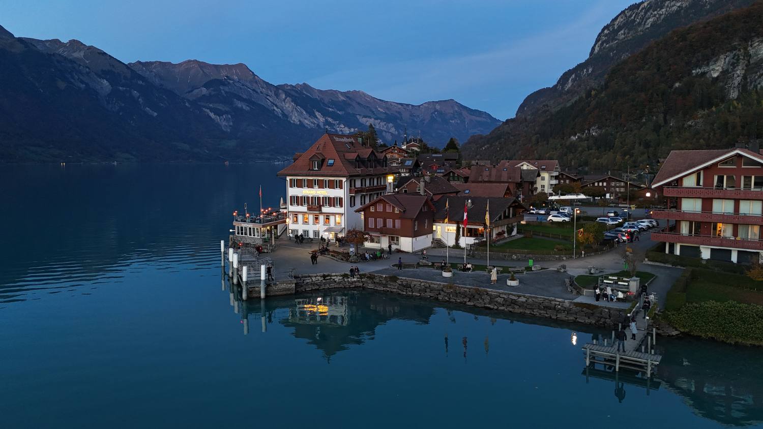 The harbour of Iseltwald on Lake Brienz at dusk, with lit windows reflected in the water
