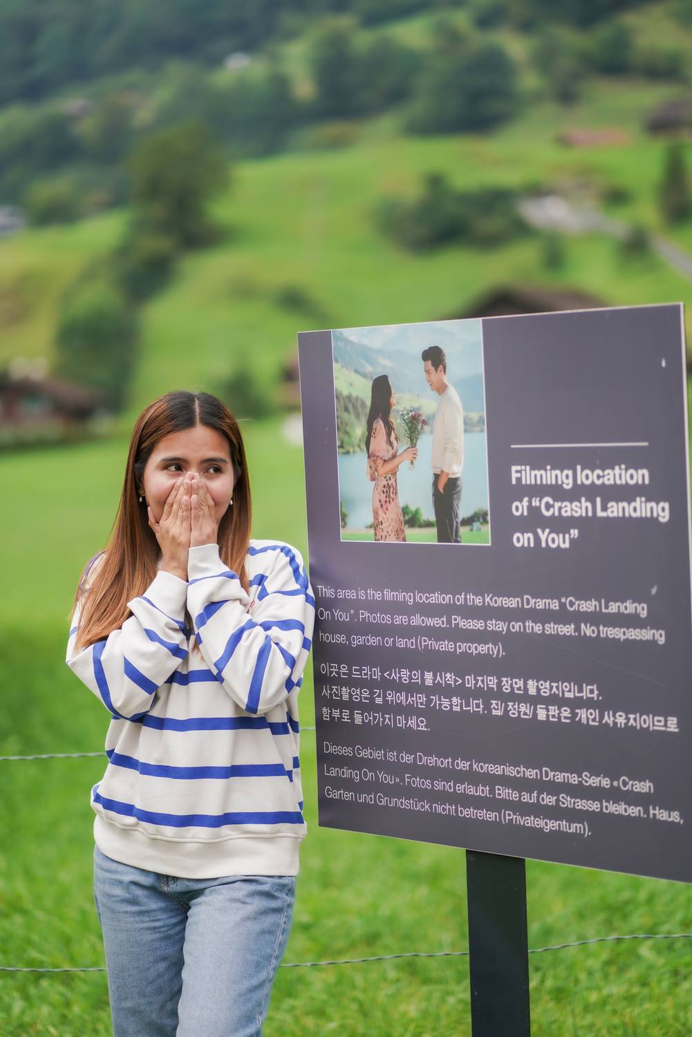 A guest beside the sign marking the Crash Landing on You filming spot at Iseltwald