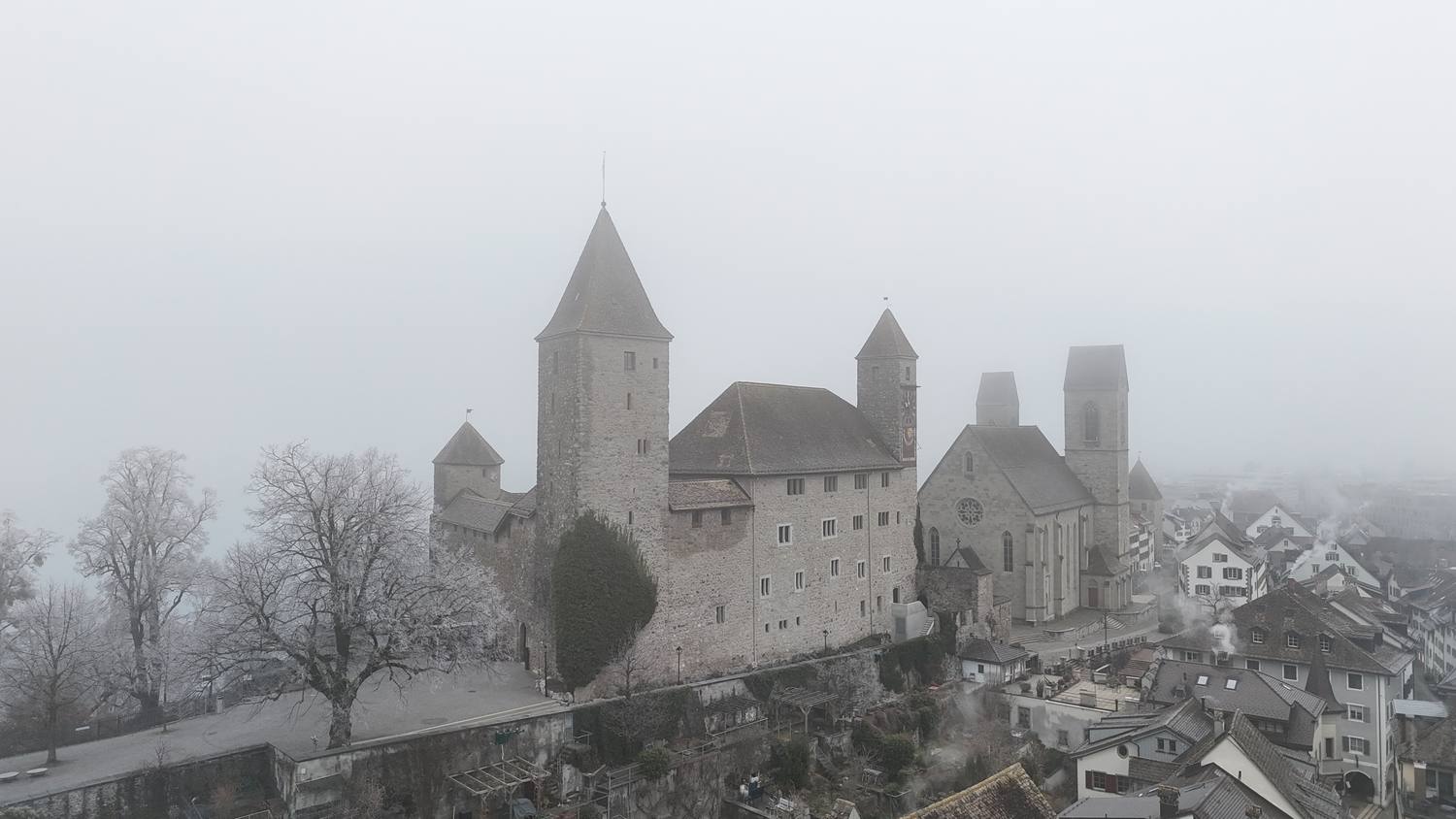 Rapperswil Castle and the parish church above the old town roofs on a foggy winter morning