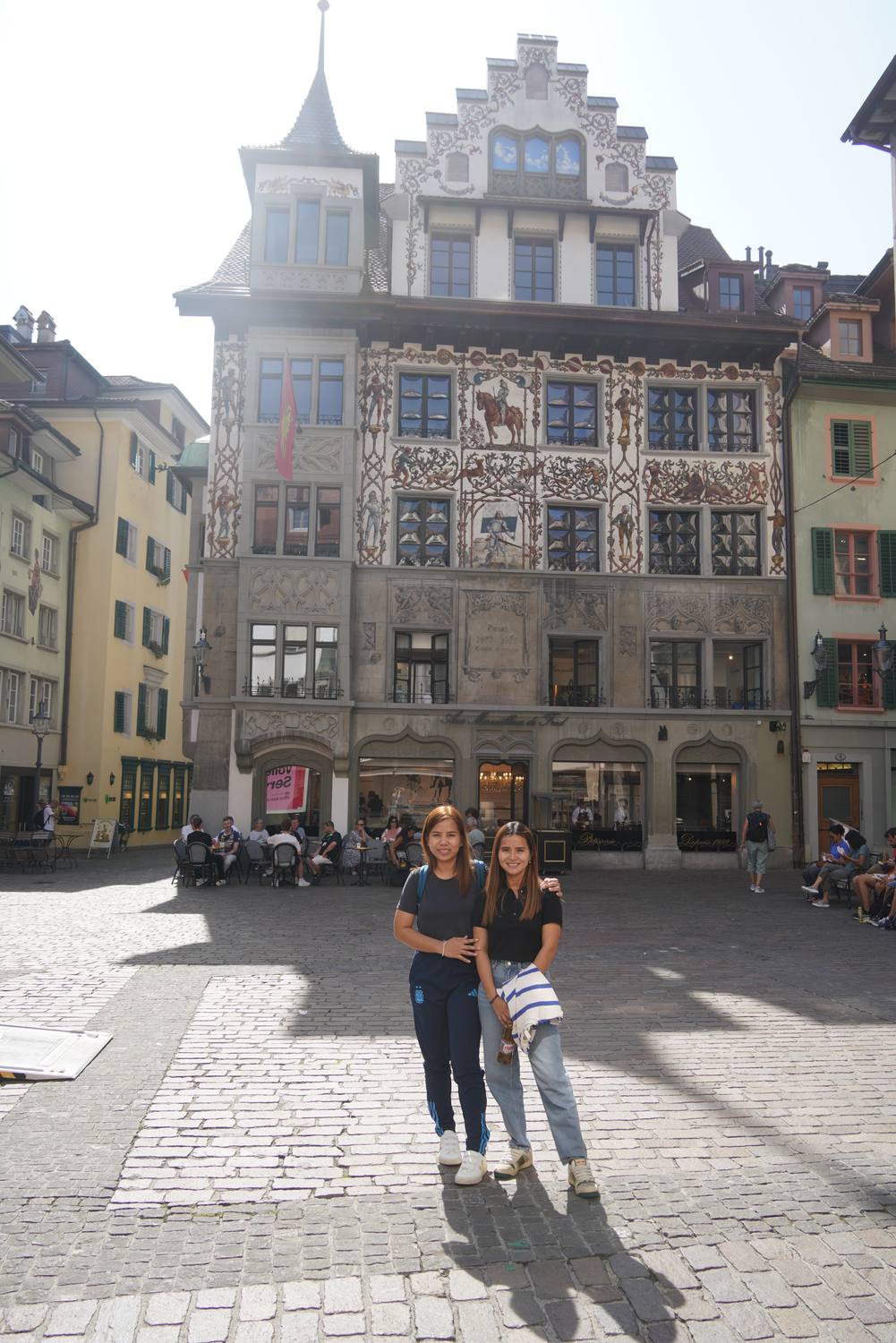 Two guests on a square in Lucerne old town in front of a richly painted house front