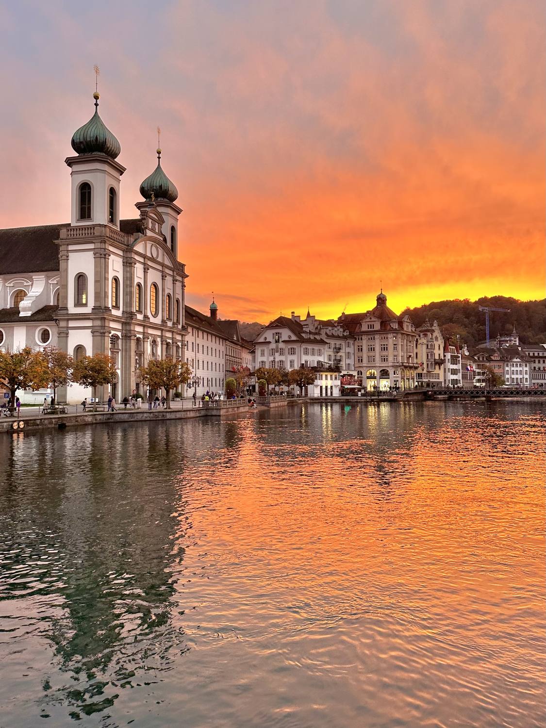 The Jesuit Church in Lucerne mirrored in the Reuss under an orange sunset