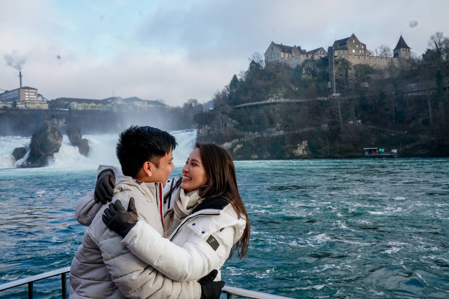 A couple embracing on the viewing platform at the Rhine Falls, Schloss Laufen on the cliff behind