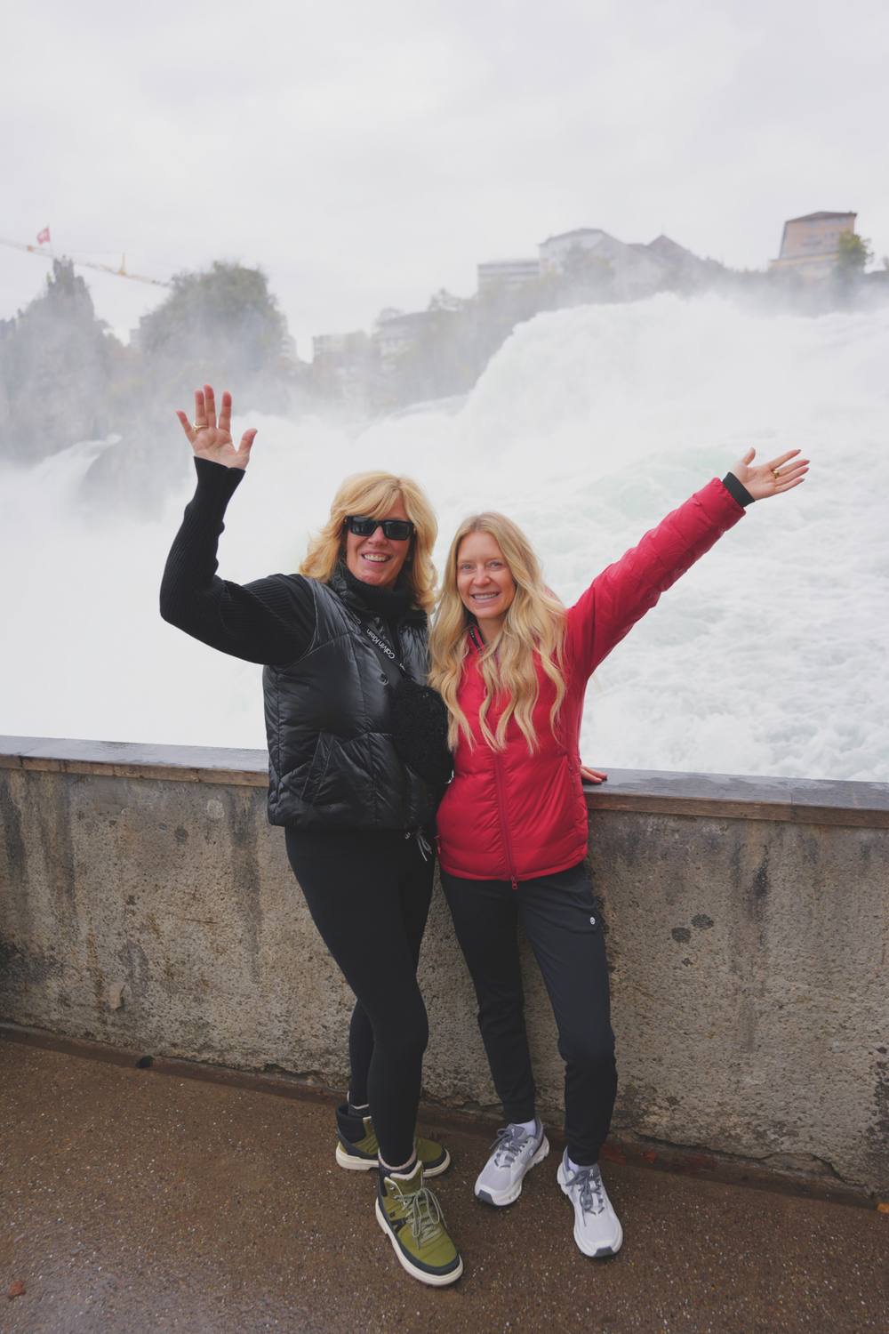Two guests on the viewing platform at the Rhine Falls, spray rising behind them