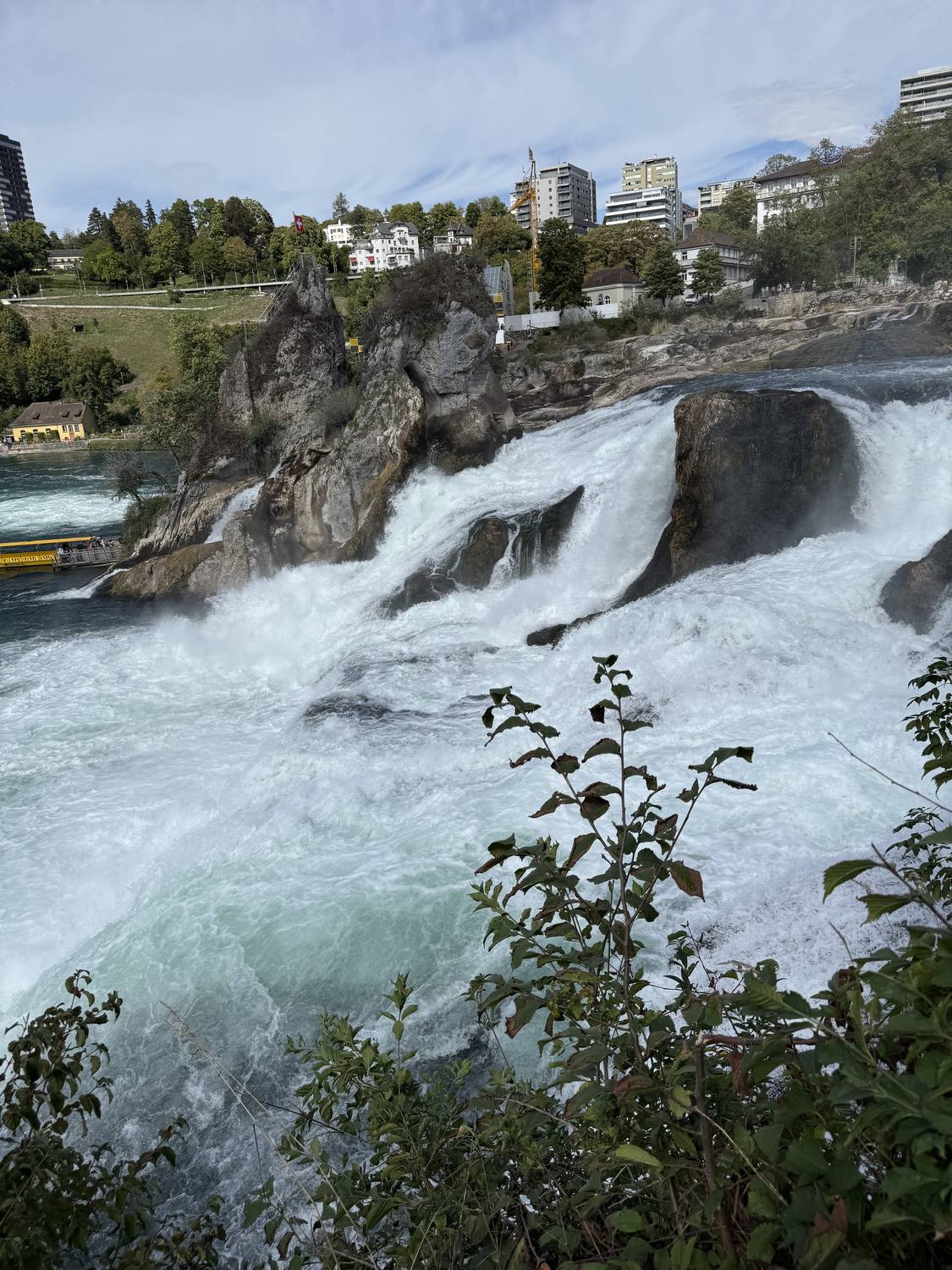 The spray at the foot of the Rhine Falls, with Neuhausen on the bank above