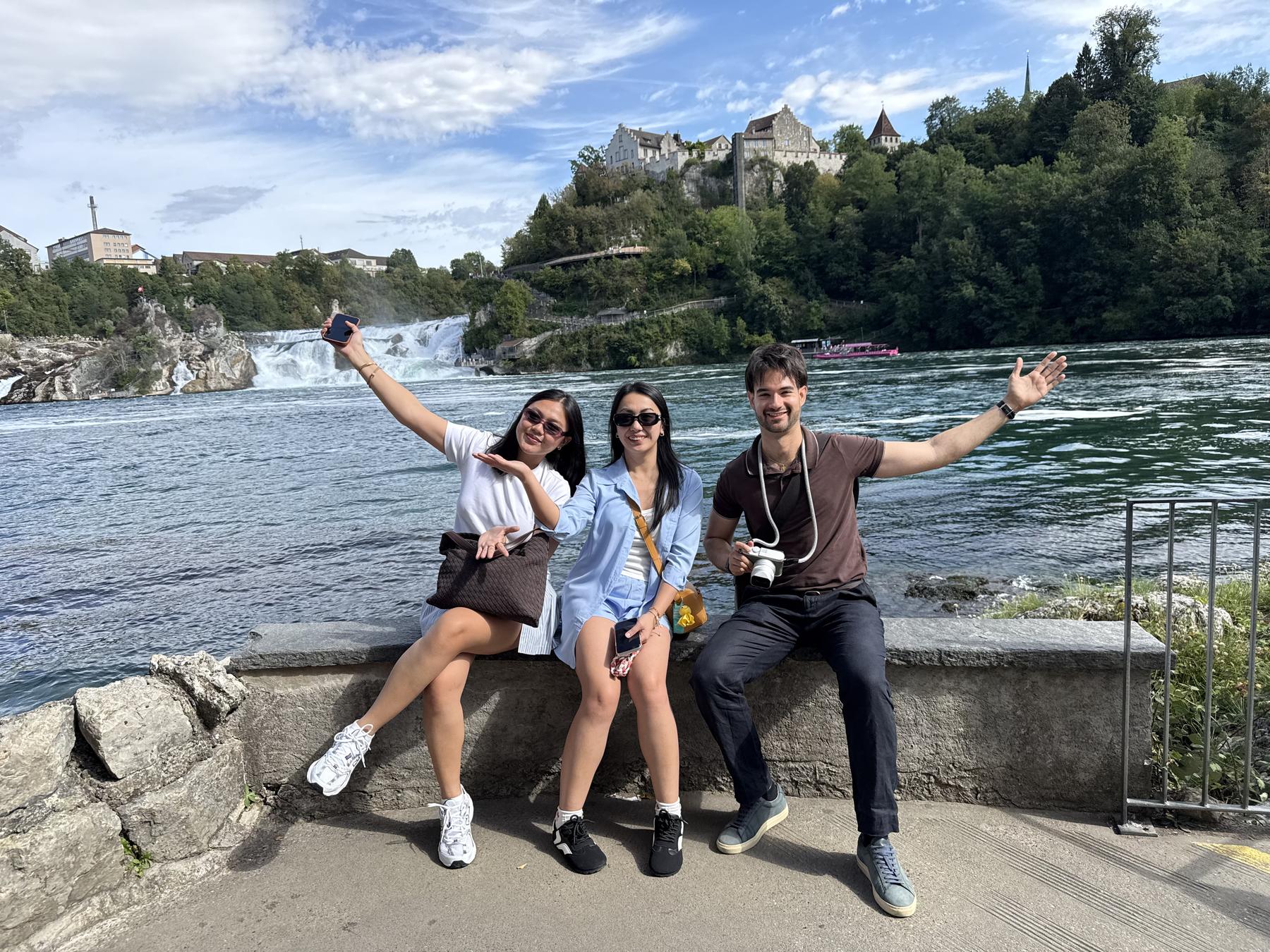 The Creative Tour team on the bank of the Rhine at the Rhine Falls, with Schloss Laufen on the cliff behind them
