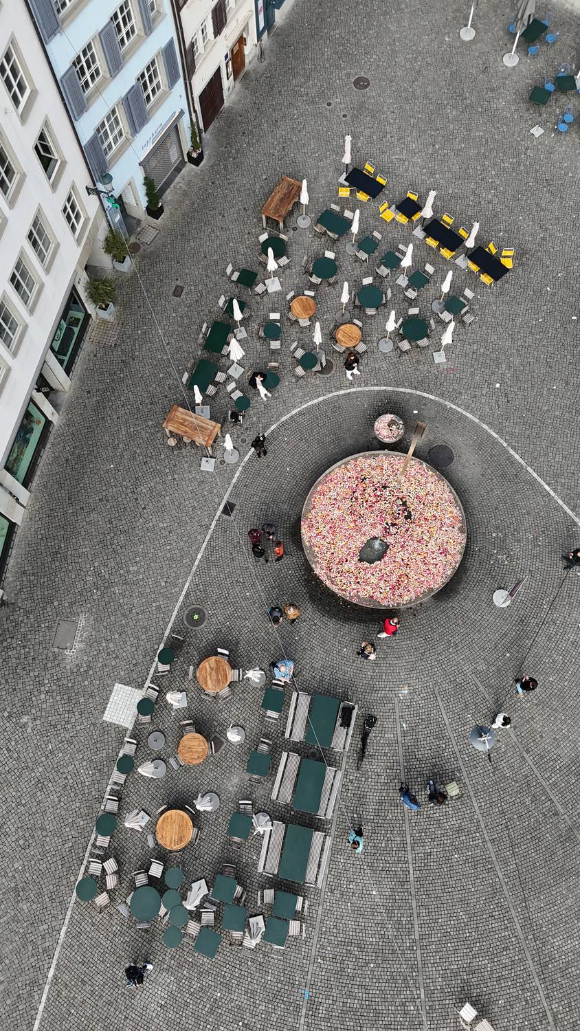 Café tables around the flower-filled fountain on Münsterhof in Zurich, seen from directly above