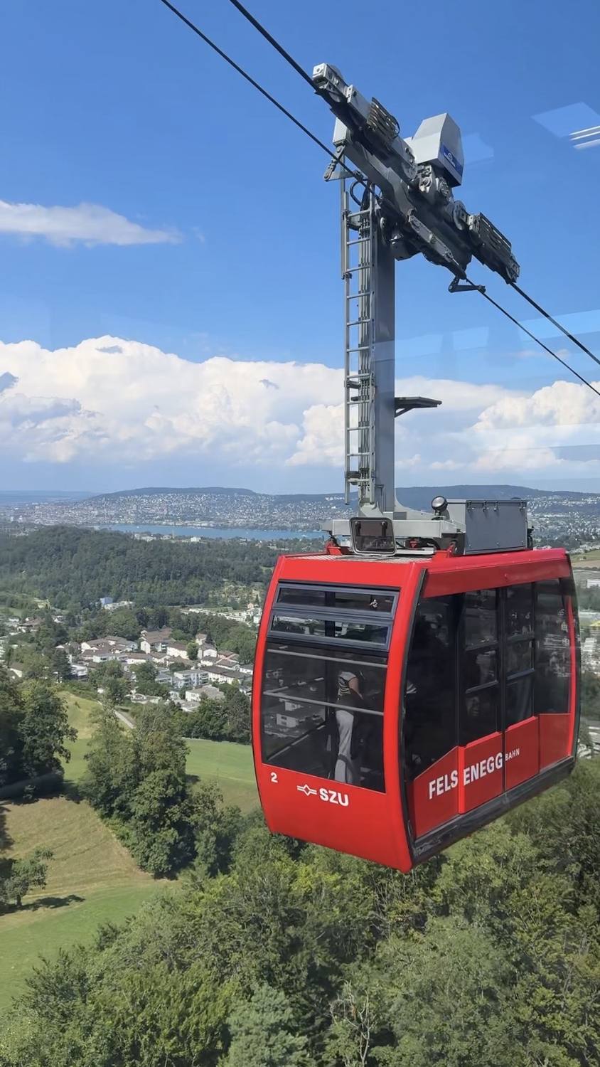 The red Felsenegg cable car above the Sihl valley, with Zurich and its lake behind